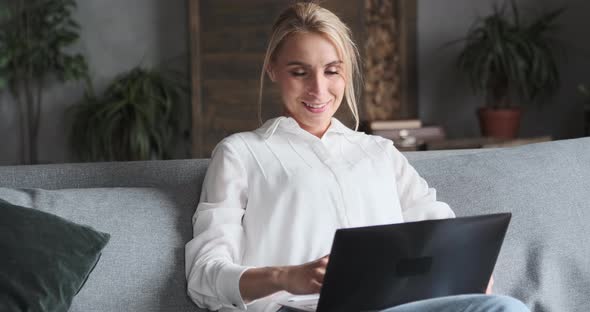 Happy Cute Blonde Woman Chatting Surfing Internet Use Laptop Sitting on Couch at Home Office