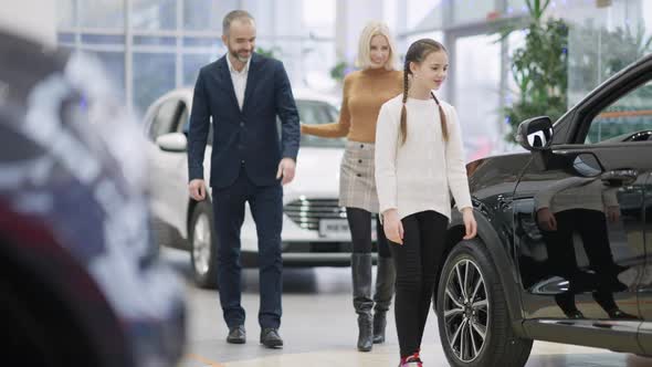 Wide Shot of Girl Choosing Car in Dealership with Couple of Parents