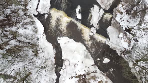 Aerial top-down drone view of a flowing stream in winter with snow covering the land around it. Reco