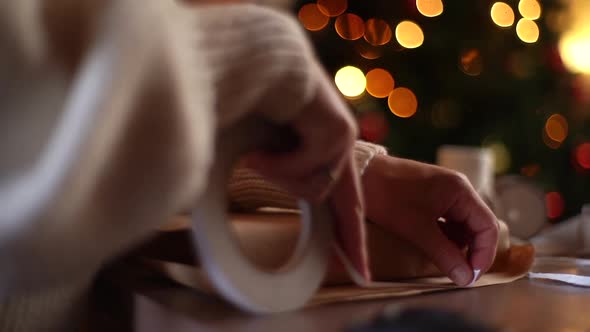 Closeup of Unrecognizable Young Woman Applying Doublesided Tape to Craft Wrapping Paper to Package