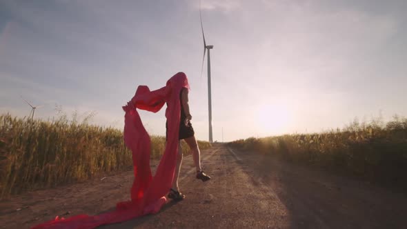 Woman with Pieces of Red Cloth Run to the Wind Generator in the Field