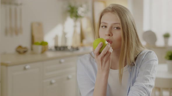 Woman is Throwing Up Apple and Eating It Looking at Camera Posing Alone Sitting on Chair in Kitchen