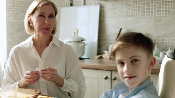 Adult Woman Communicates in the Kitchen at the Table with a Teenager Smiling