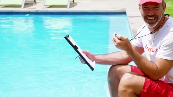 Lifeguard sitting at pool side holding clipboard and stop watch