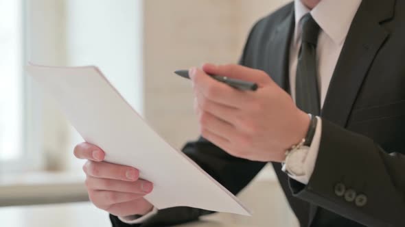 Close Up of Middle Aged Businessman Holding Papers and Pen Studying Report