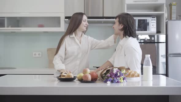 Side View of Laughing Young Caucasian Couple Standing on Kitchen and Talking. Portrait of Beautiful