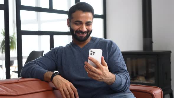 Happy Young Bearded Indian Eastern Man Holding Cellphone and Waving Hello
