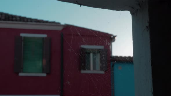 A closeup of a spiderweb on a stone opening in front of a blurred Burano facade