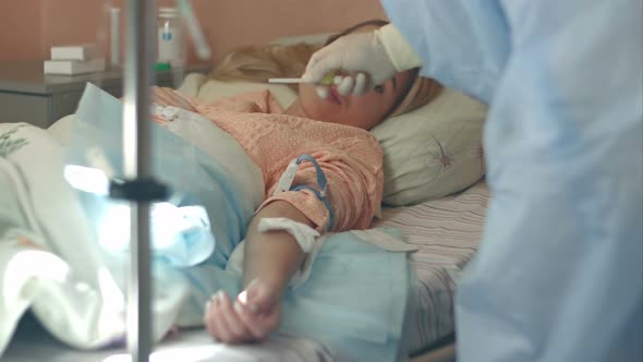 Nurse in Gloves and Mask Putting Female Patient on a Drip in a Hospital Ward