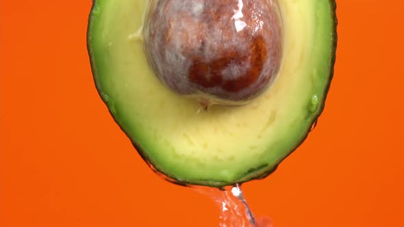 Water falling from avocado on orange background. Avocado slice and water splashing, drops of juice