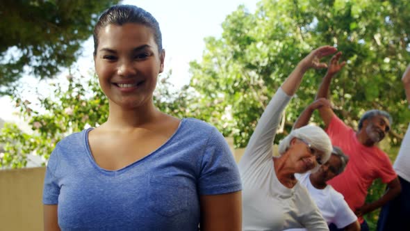 Trainer smiling at camera while seniors exercising in background 4k