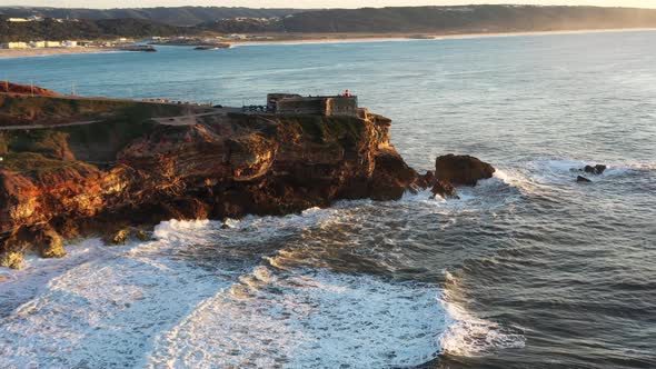 The Nazare Portugal Lighthouse in Praia do Norte during golden hour sunset, Aerial dolly in from sid