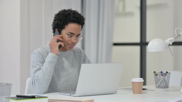 African Woman with Laptop Talking on Smartphone