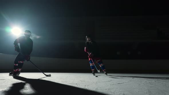 Two Sportsmen Hockey Players Who are Sliding on Ice Arena and Dribbles Hitting Puck with Stick