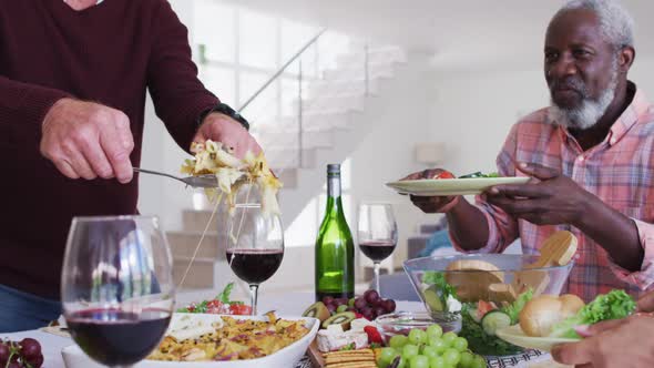 Diverse senior couples sitting by a table drinking wine and eating dinner