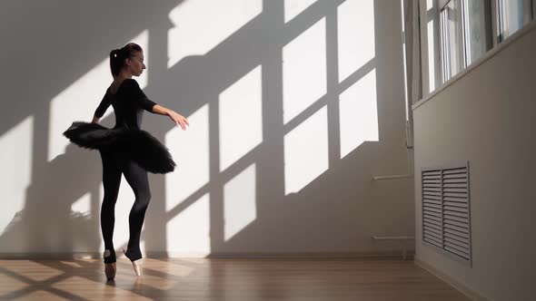 Ballerina in Black Tutu Gracefully Dances Against White Wall in Bright Sunlight