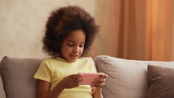 Portrait Little African American Girl in Plays a Game on Smartphone