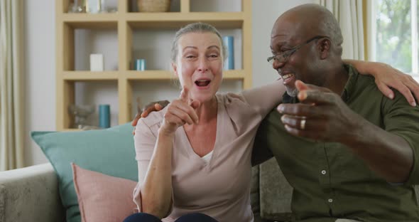 Portrait of happy senior diverse couple wearing shirts and making video call in living room
