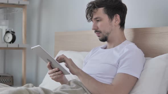 Young Man Using Tablet While Lying in Bed