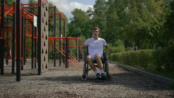 Wide Shot Young Tired Caucasian Man in Wheelchair on Sports Ground in Park Looking Away Talking and