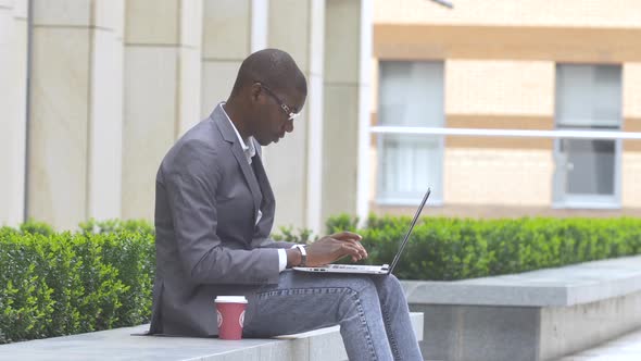 American Businessman Working with Glasses on Laptop Outdoors on a Background of Corporate Building