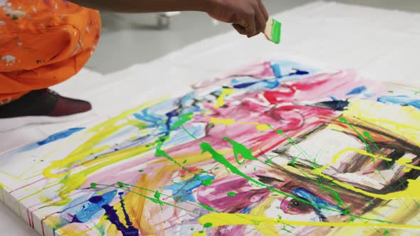 Close up of african american male artist pouring paint with a paint brush on canvas at art studio