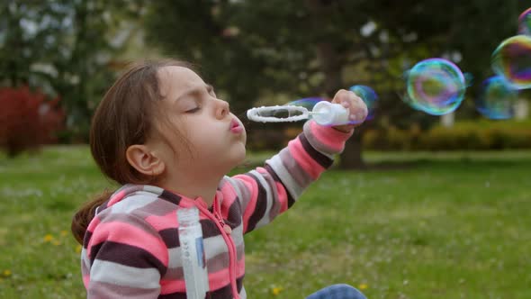 Little Cute Girl is Playing Outside Blowing Soap Bubbles