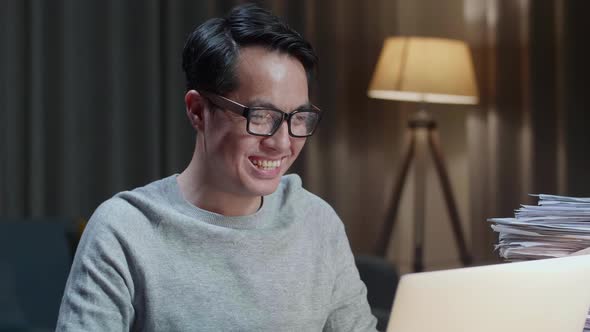 Close Up Of Asian Man Having Video Call On Laptop While Working With Documents At Home