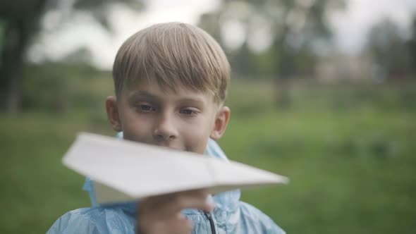 Closeup Portrait of Charming Caucasian Schoolboy Launching Paper Plane Outdoors