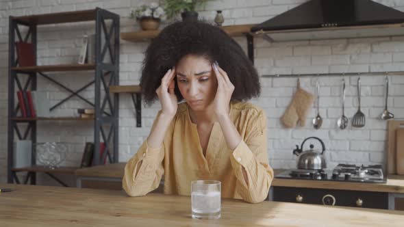 Afro-American Girl Sits at the Table with a Headache. She Sits and Touches Her Temples. She Has Her