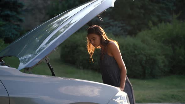 Young Upset Woman Standing at Broken Car Worrying in Stress