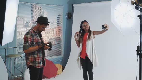 Pretty Black Model Making Selfie on Smartphone During Photo Shoot in Modern Studio