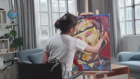 Asian Artist Girl In Wheelchair Holding Paintbrush Mixed Colour And Painting A Girl On The Canvas