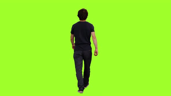 Rear View of Casual Man in Black T-shirt Walks on Green Background