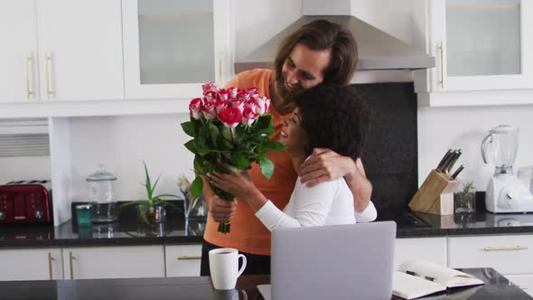 Caucasian man giving a flower bouquet to his wife in the kitchen at home