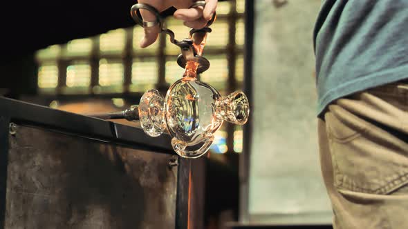 Glass artist cuts off section of molten glass during the glass blowing process.