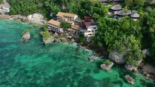 tropical turquoise ocean coastline in Uluwatu Bali with hotel on cliff, aerial