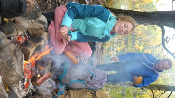 Young Woman Fry Sausages on an Open Fire in the Woods. A Vertical Video.