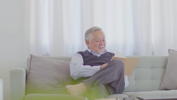 Happiness Asian Elderly man with white hairs sitting on sofa reading book enjoy relax