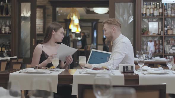 Young Beautiful Woman Sit with Papers on the Table in Restaurant with a Mature Bearded Man