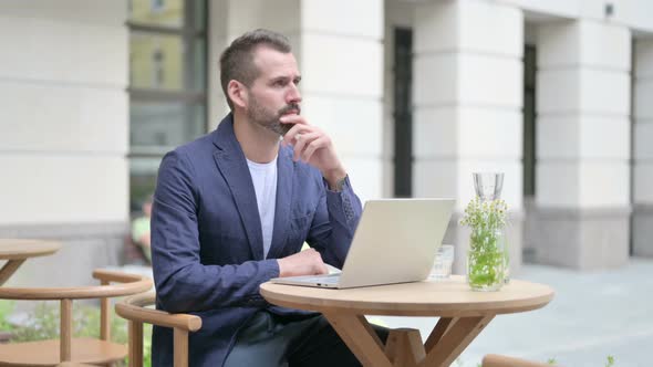 Man Thinking While Using Laptop Sitting in Outdoor Cafe