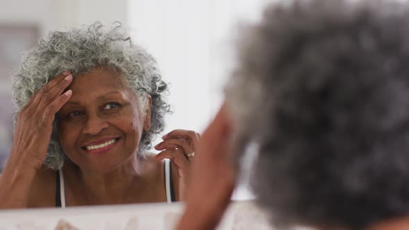 Senior african american woman touching her hair while looking in the mirror at home