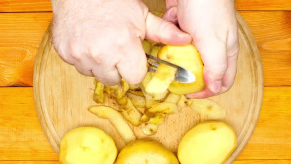 The cook is peeling potatoes. A man peels raw fresh potatoes with a manual potato peeler. Peeled