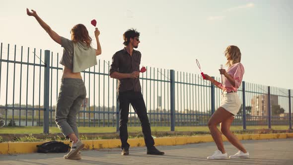 Three Friends Have Fun on the Street Make Soap Bubbles and Eat Lollipop at Sunset