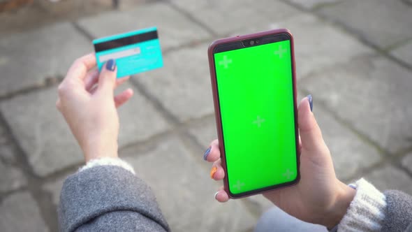 Smartphone and credit debit card in hands of girl smartphone green screen for chroma key on street