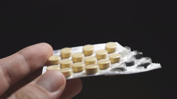 Close-up of a Man's Hand on a Dark Background Holding a Pack of Pills on a Blister. Covid-19