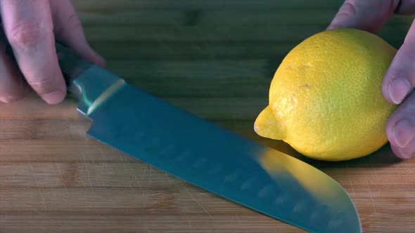 Slicing a Fresh Lemon with a Chefs Knife on a Wooden Chopping Board in the Kitchen