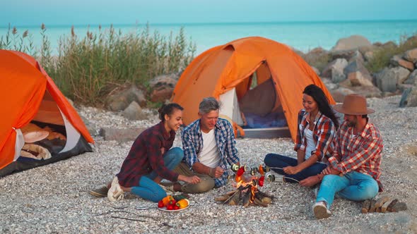 Two Lovely Couples Traveling with Tents and Grilling Vegetables on Bonfire for Dinner