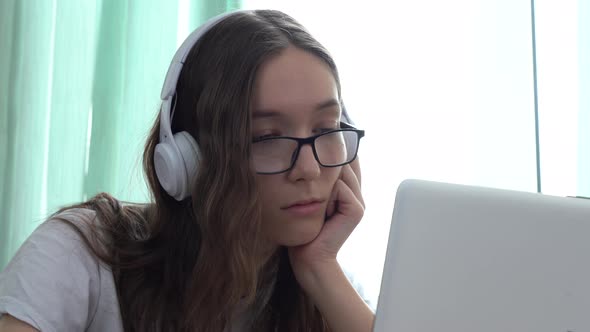 Serious Caucasian Girl Wearing Headphones and Watching an Educational Video Course with Her Laptop