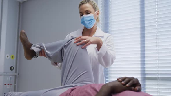 Diverse female orthopedic doctor examining male patient in face masks